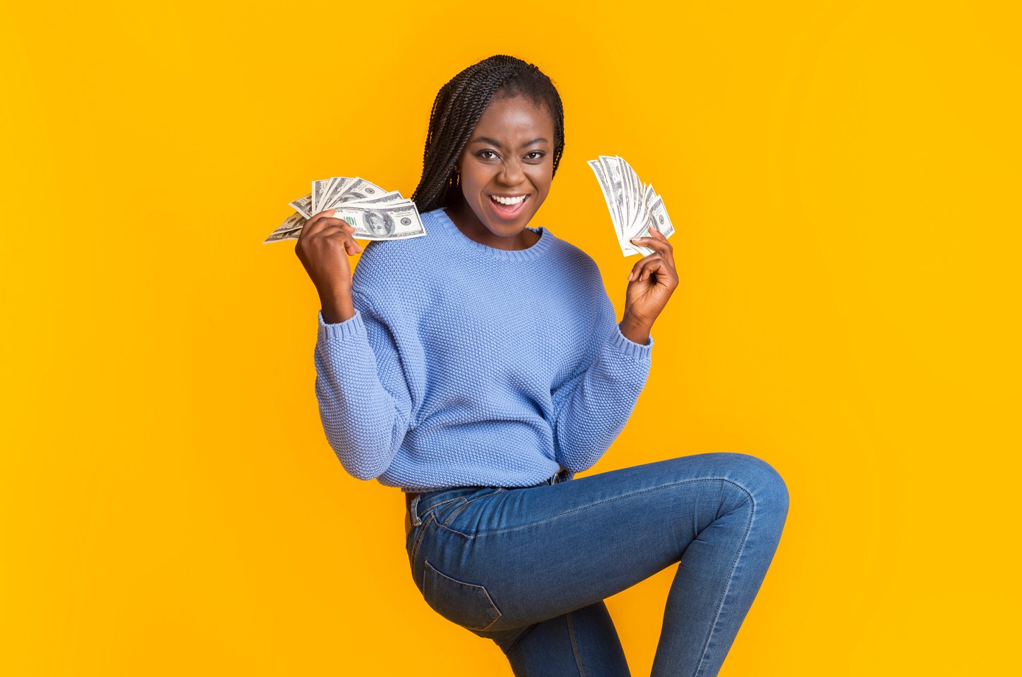 Extremely happy young black woman holding money in both hands